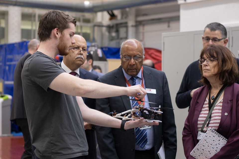 A student demonstrating a robot to visitors at a public event.