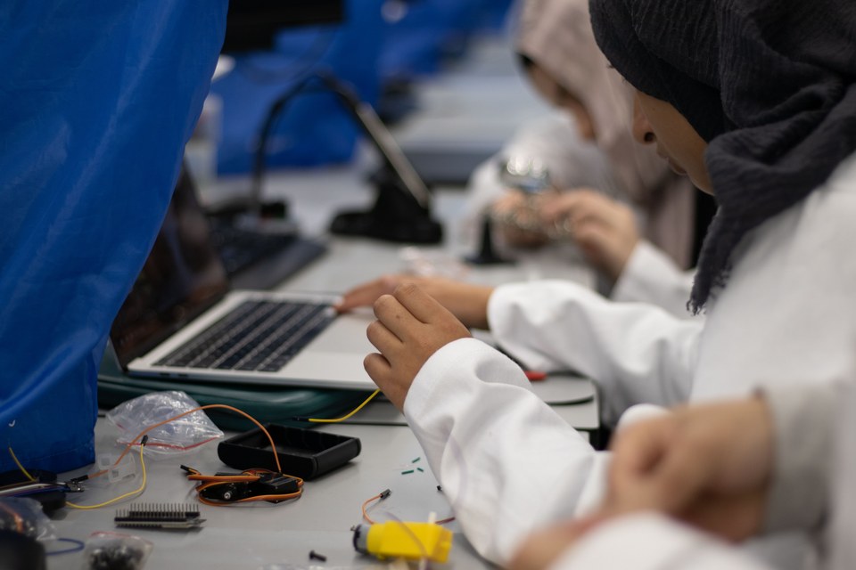 Students working with tools and electronics across a shared bench.