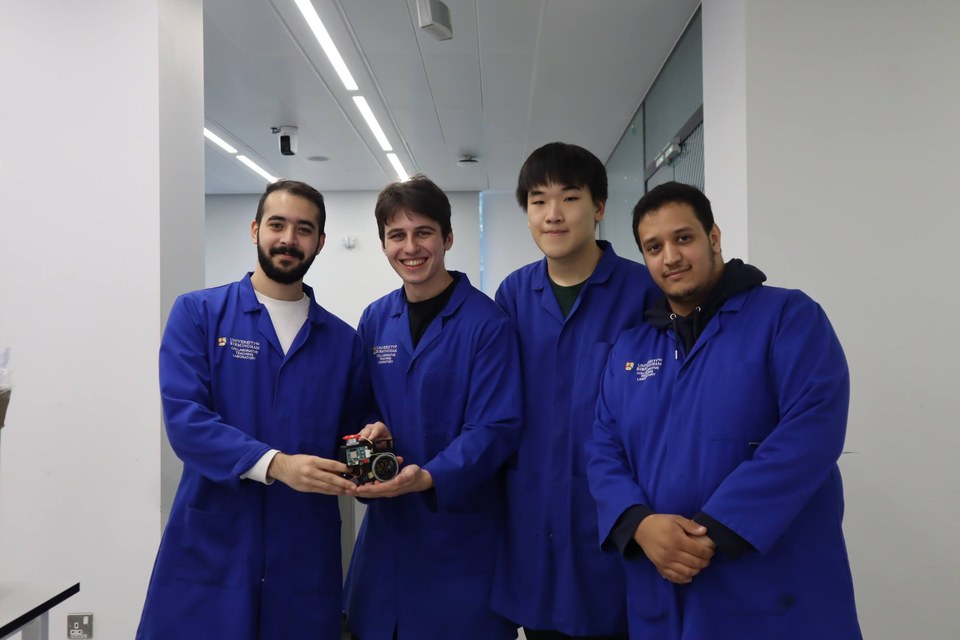 Four students in blue laboratory coats presenting a small completed project.