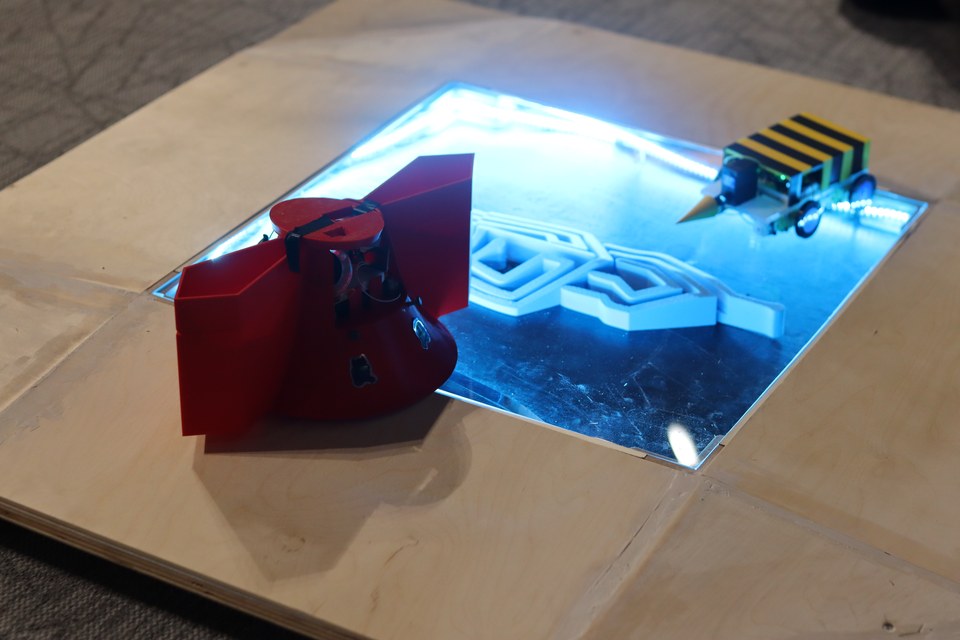 A red student-built robot positioned at the edge of an illuminated arena.