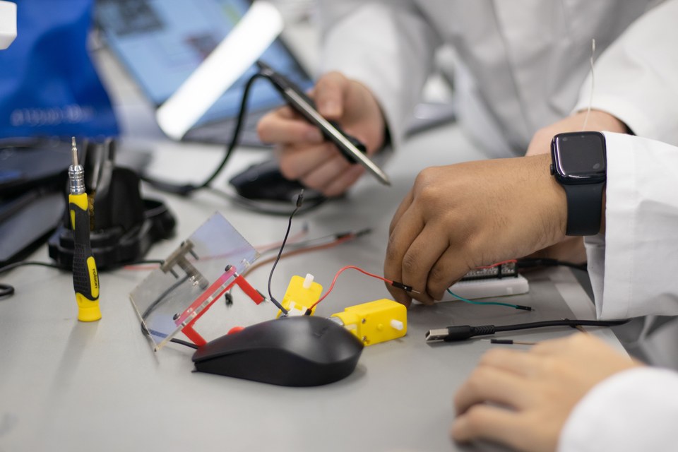 Students assembling small mechanical and electronic parts at a bench.
