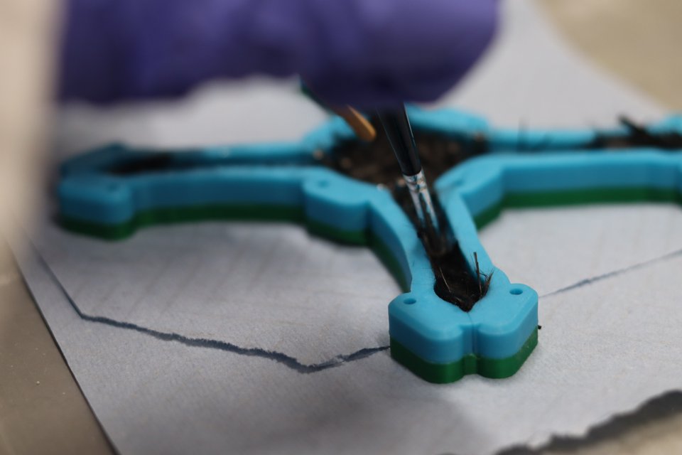 A gloved hand applying adhesive to the arm of a blue carbon-fibre drone frame.