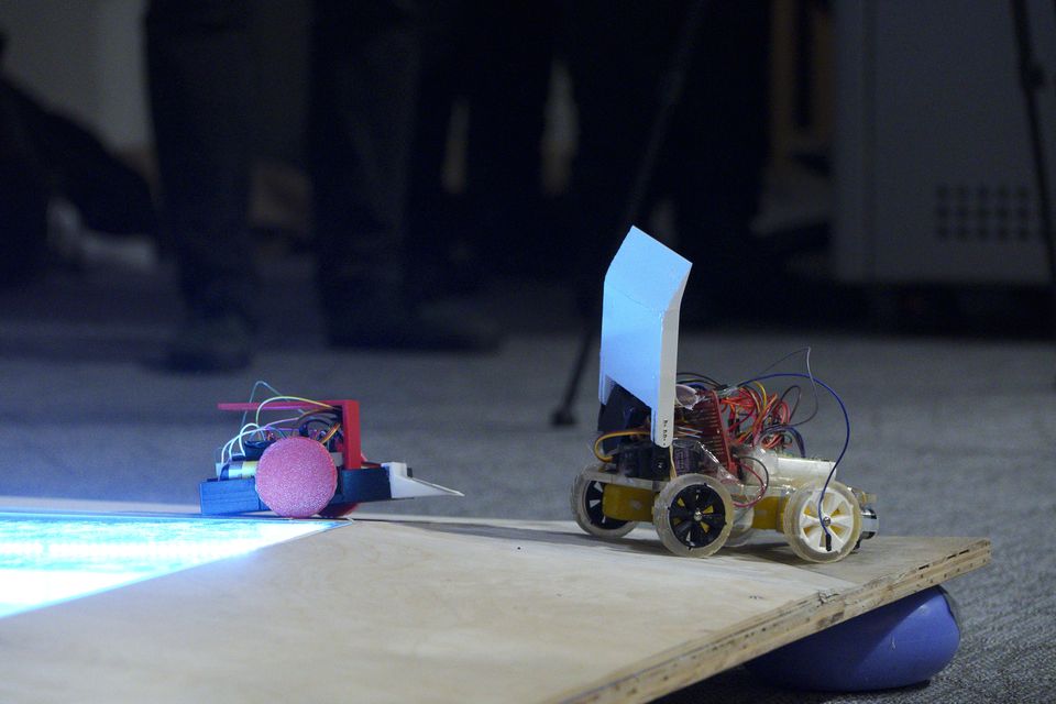 Student-built robots lined up beside a competition arena.