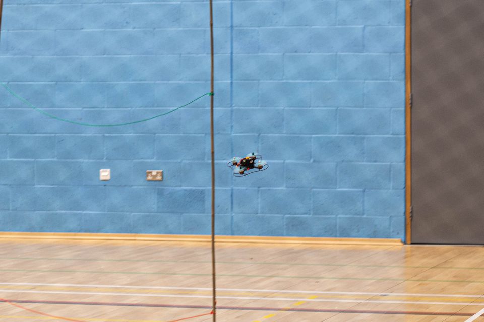 A small quadcopter flying inside a sports hall.