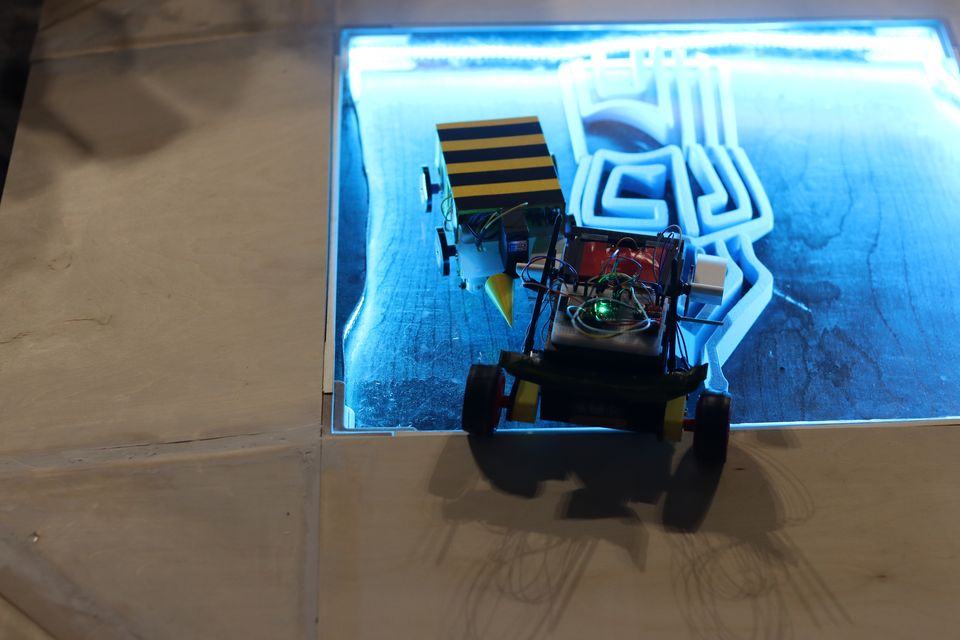 A wheeled robot crossing a cyan-lit competition mat.
