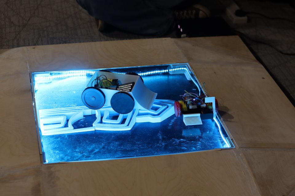 A compact robot photographed under the arena's blue lighting.