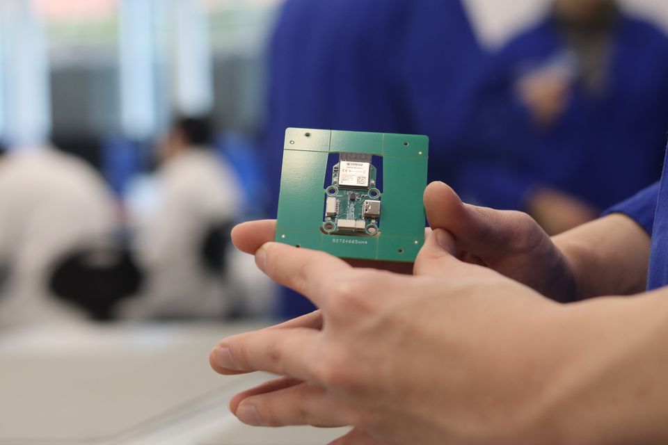 A student holding a green printed circuit board at a workbench.