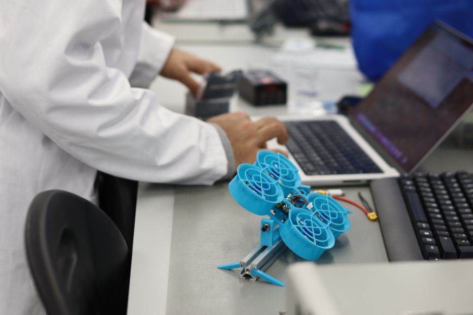 A blue ducted-fan drone frame beside a laptop in the workshop.