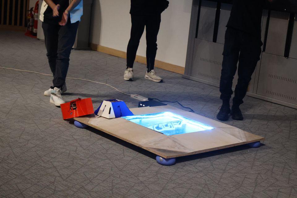 A wheeled robot moving across an illuminated event course.