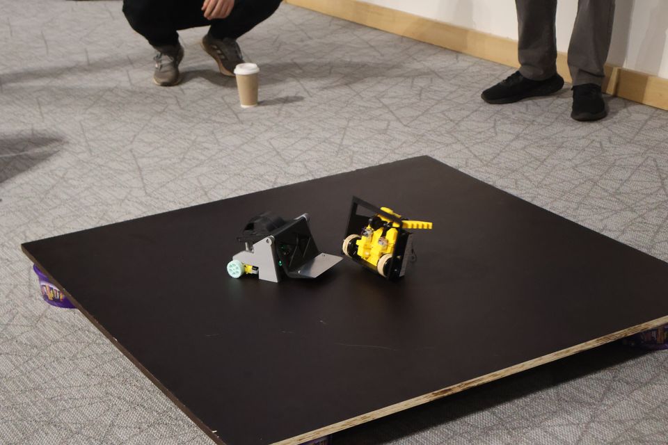Two compact robots meeting on a square competition platform.
