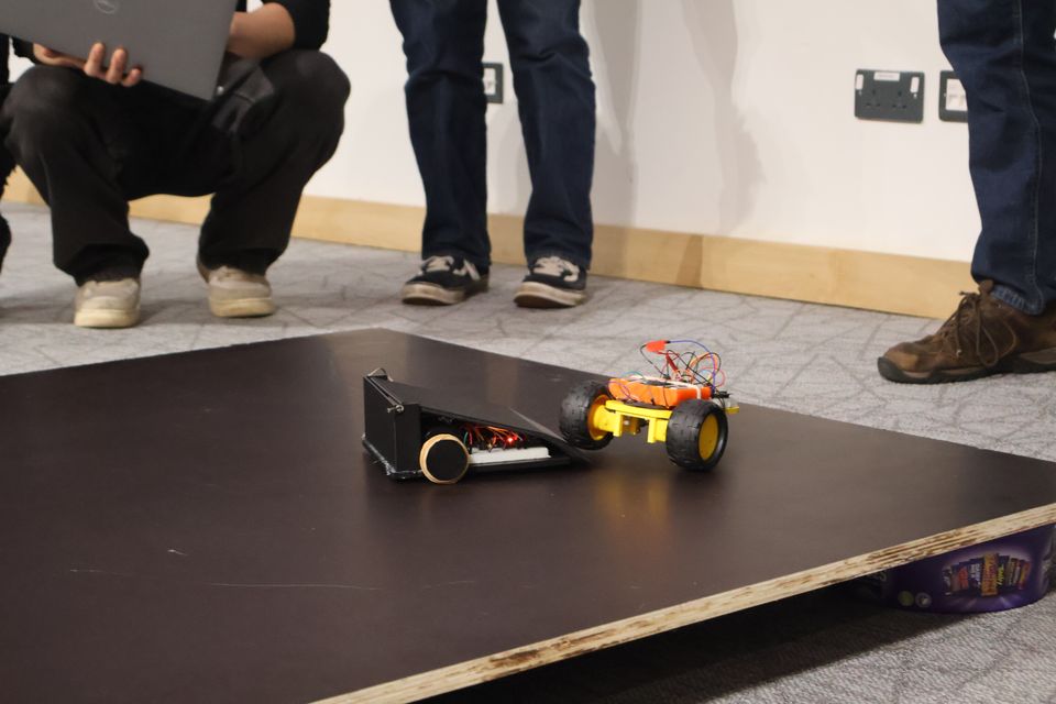 Two wheeled robots competing on a black arena surface.