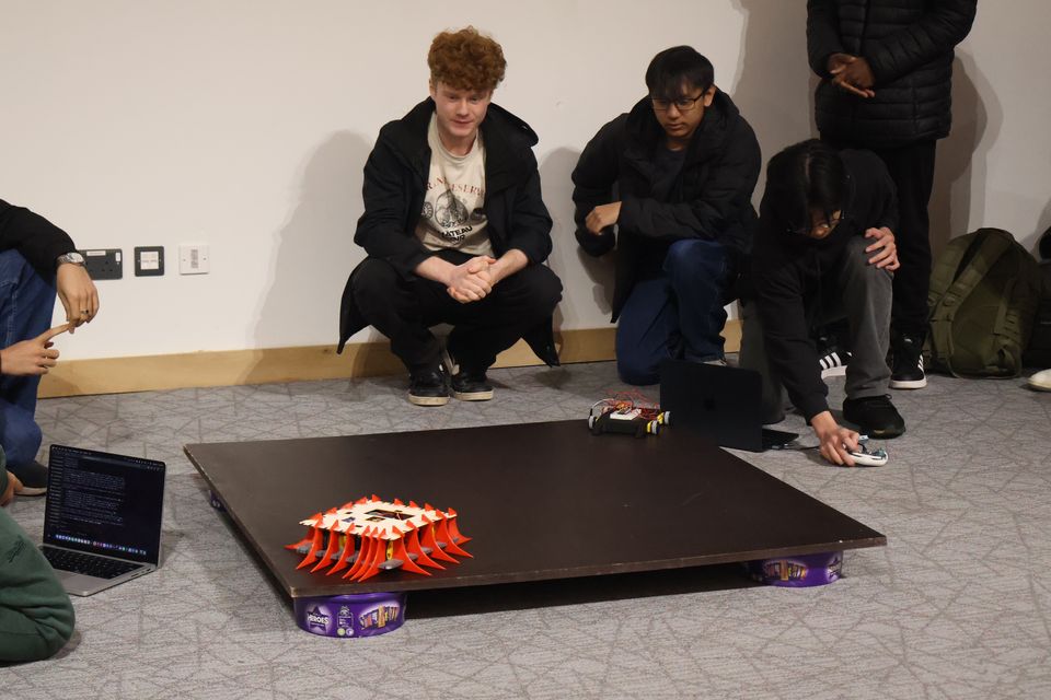 Students watching two robots compete on a tabletop arena.