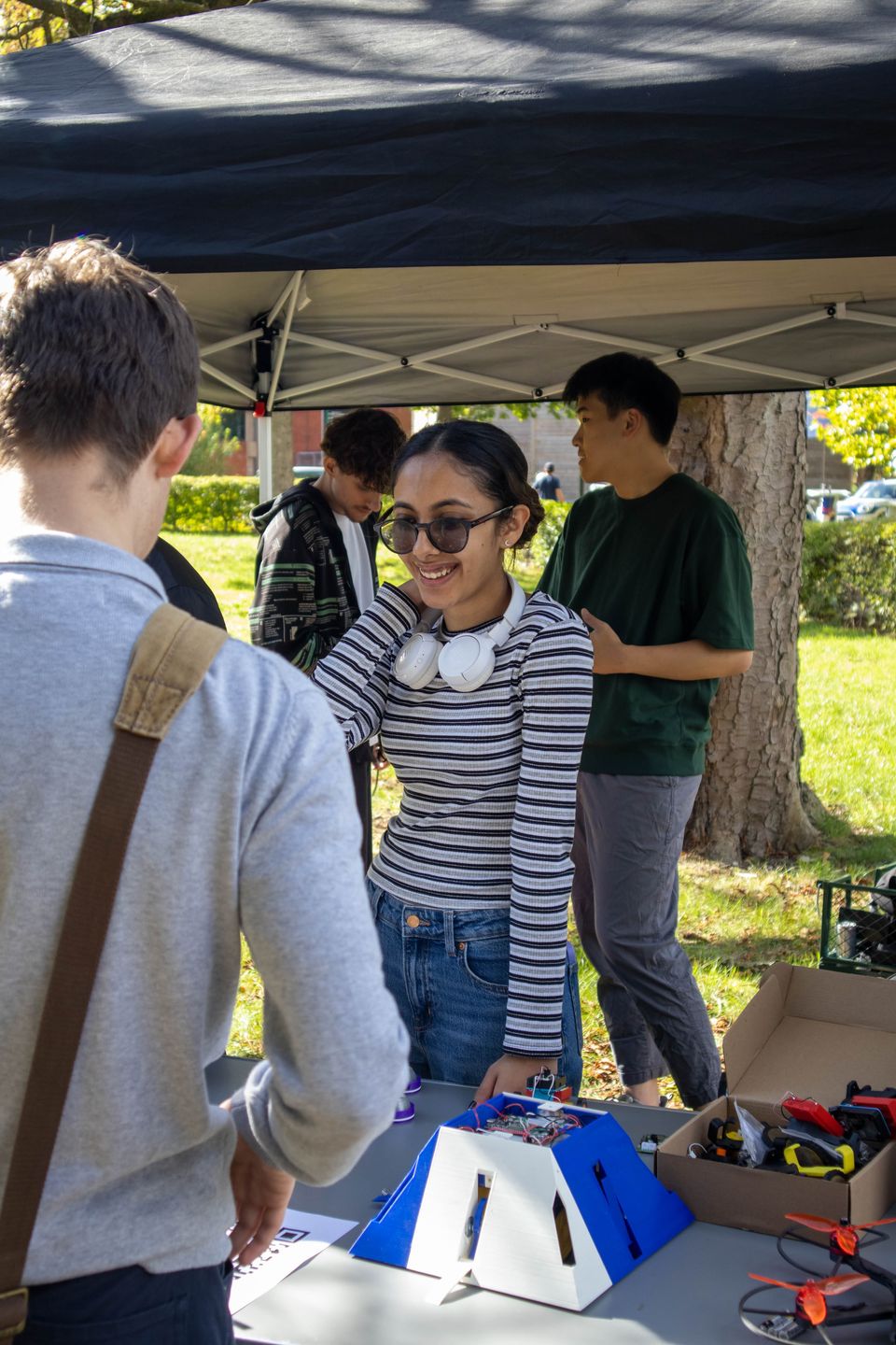 Students welcoming visitors to a UBRobotics outdoor stand.