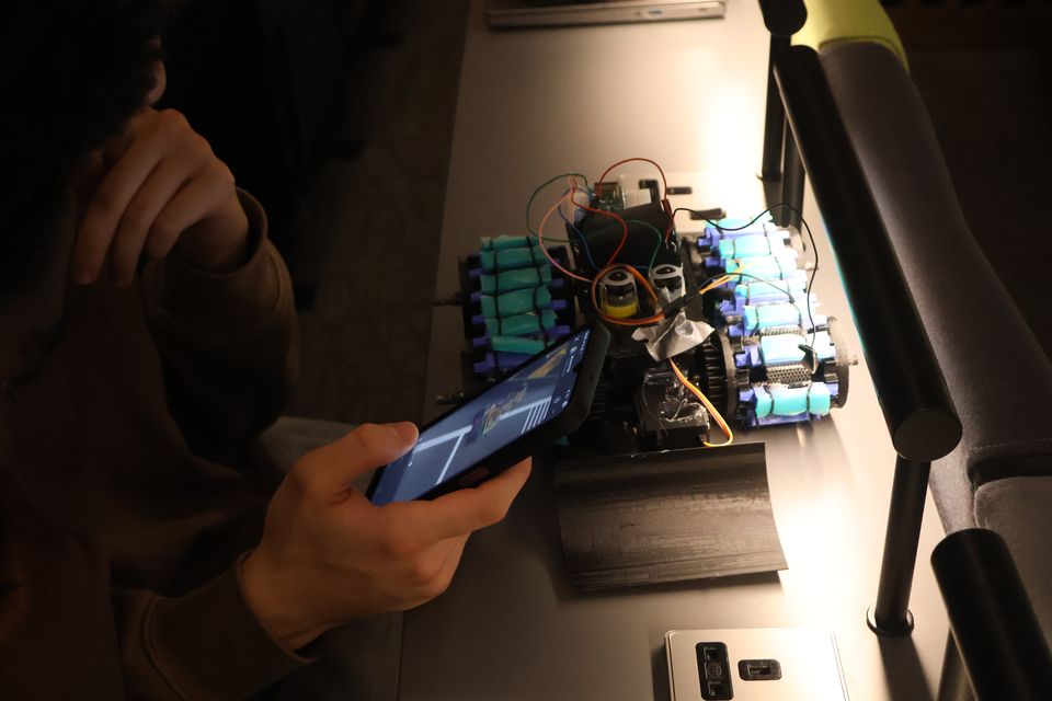 Hands making an adjustment to a wheeled robot on a workbench.