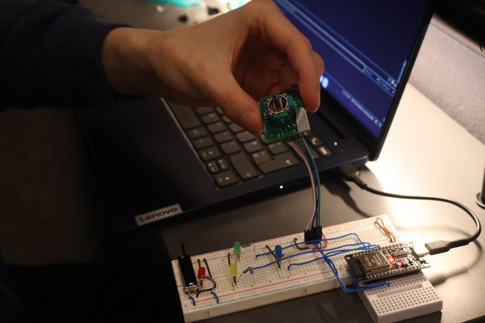 A student connecting a microcontroller beside a laptop and breadboard.