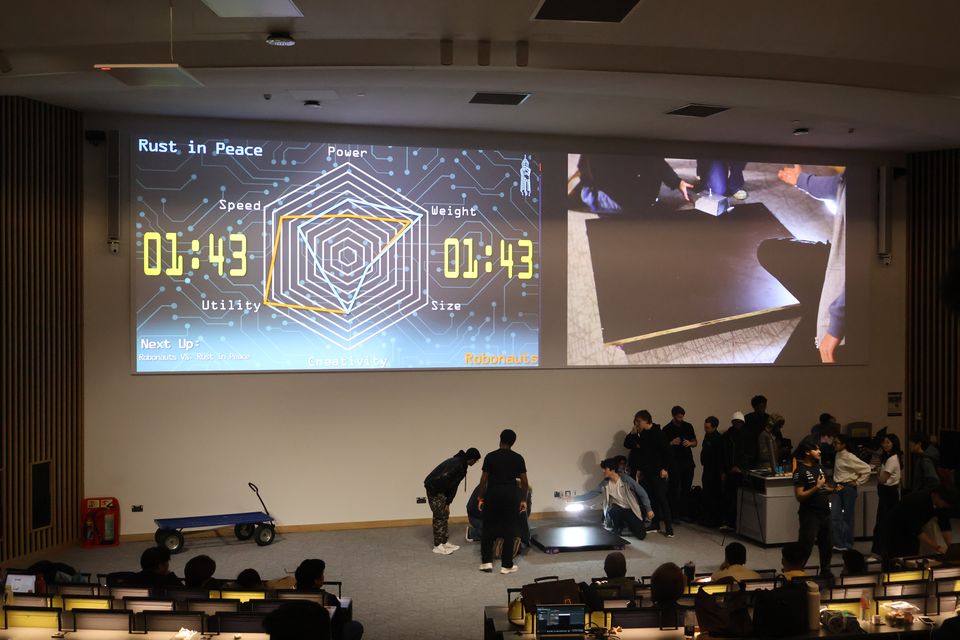 A projected match timer above a robotics arena and audience.