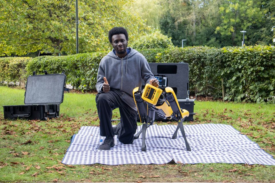 A student seated beside Boston Dynamics' Spot robot outdoors.
