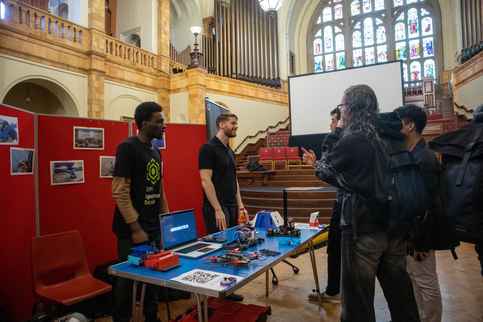 Students demonstrating robotics projects at a University event stand.