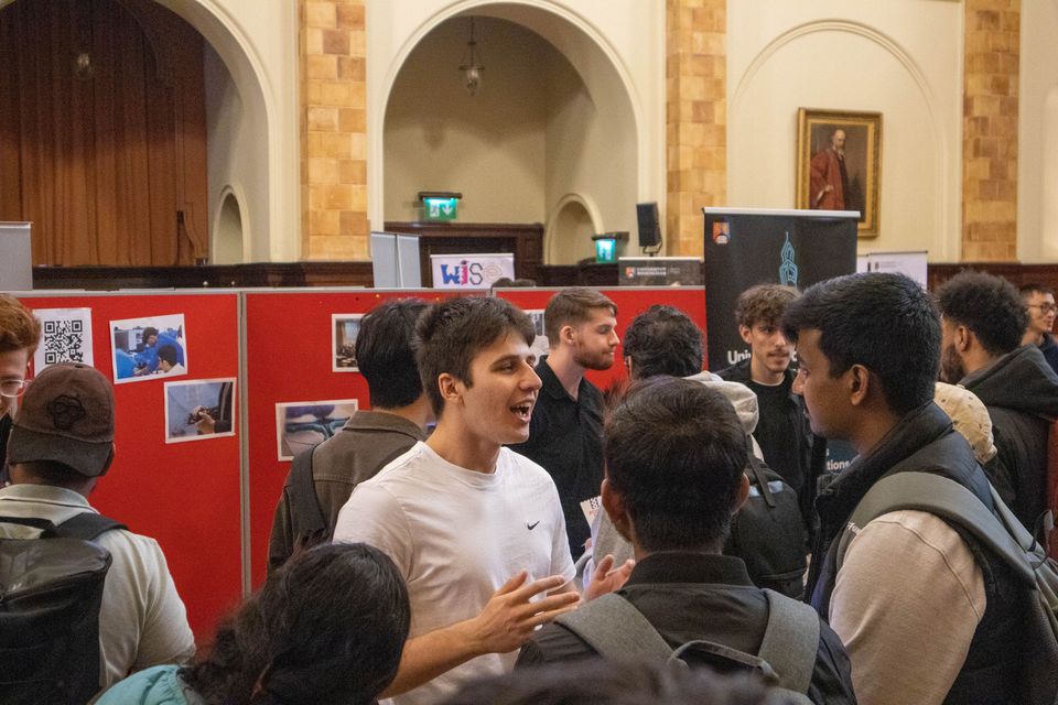 Students talking with visitors at a busy society showcase.