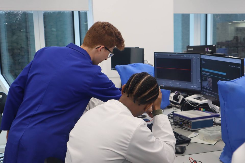 Two students in blue coats helping participants with an electronics activity.