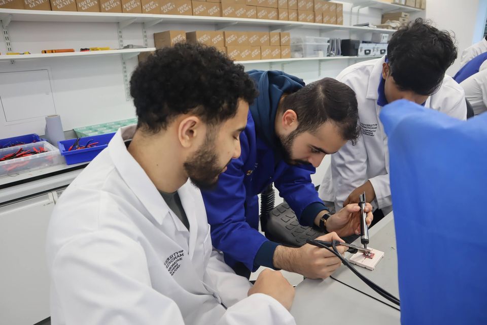 Pairs of students collaborating on electronics at a laboratory bench.