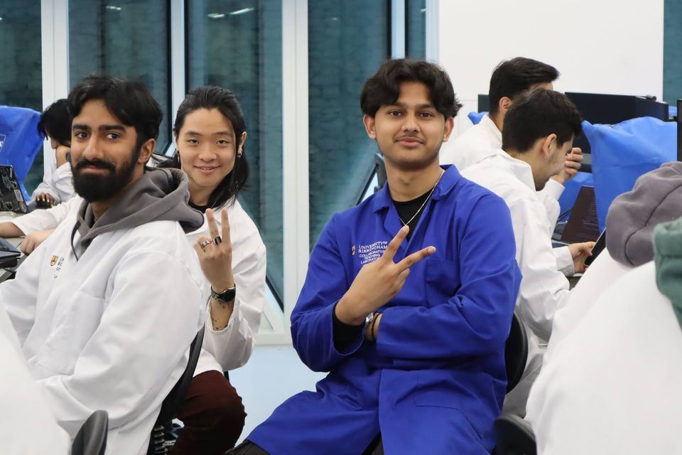Four students in blue laboratory coats holding a small project together.