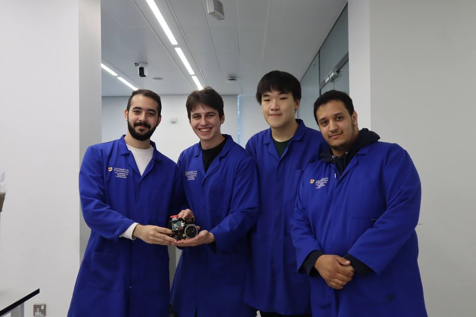 Four students in blue laboratory coats presenting a small completed project.