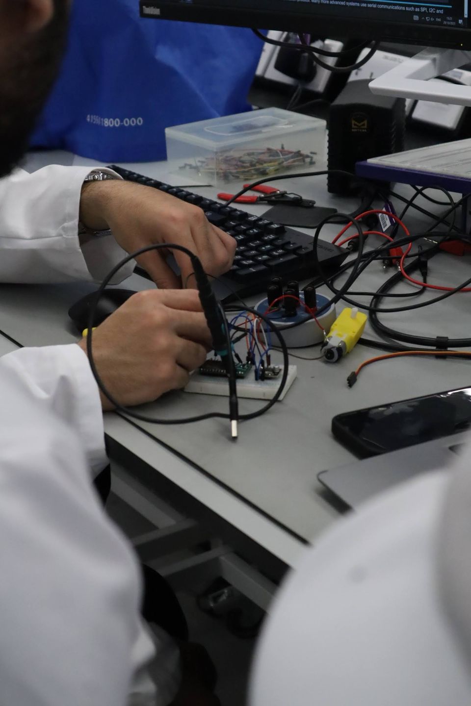 Hands using probes on an electronic circuit beside a laptop.