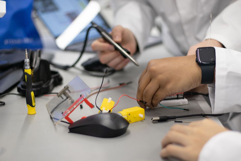 Students assembling small mechanical and electronic parts at a bench.
