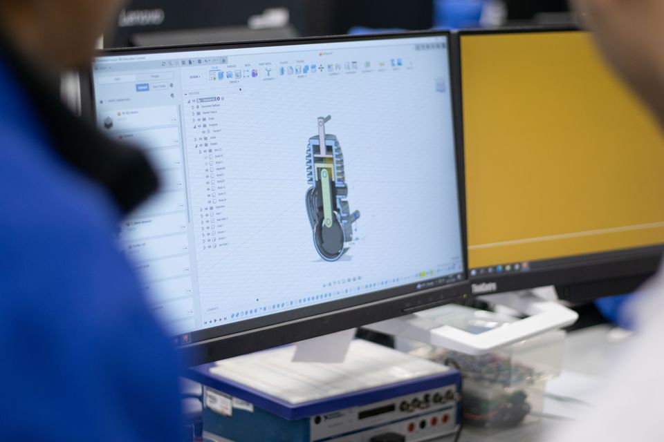 A CAD model of a wheeled robot displayed on a laboratory computer.