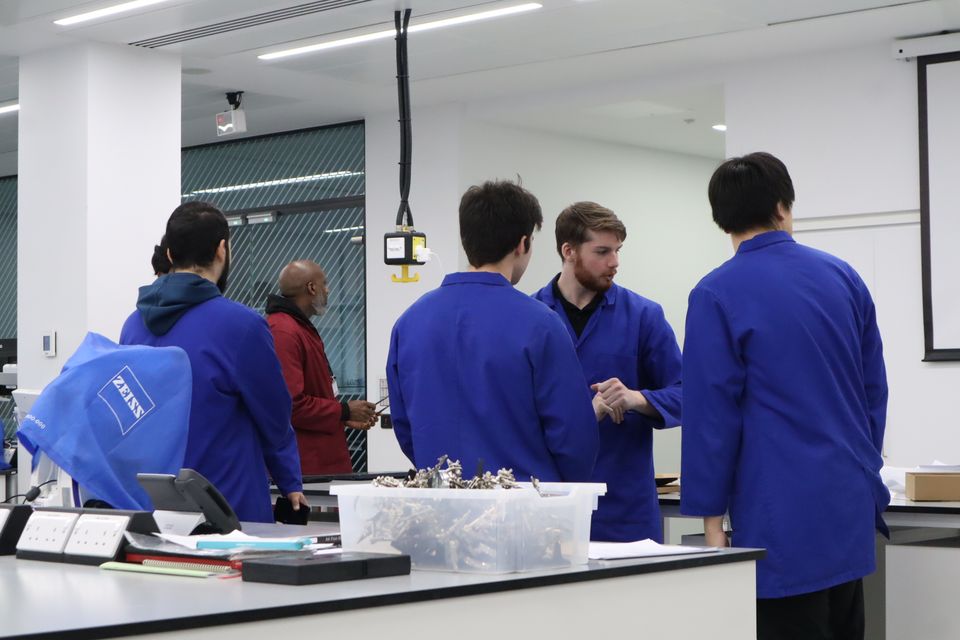 Students in blue coats supporting a busy practical session.