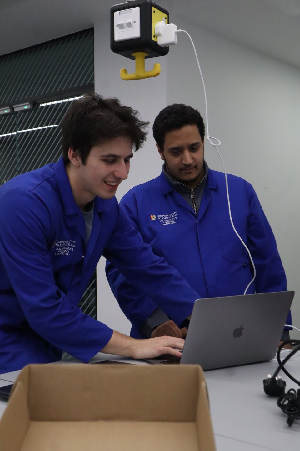 Two students in blue coats reviewing a laptop during the workshop.