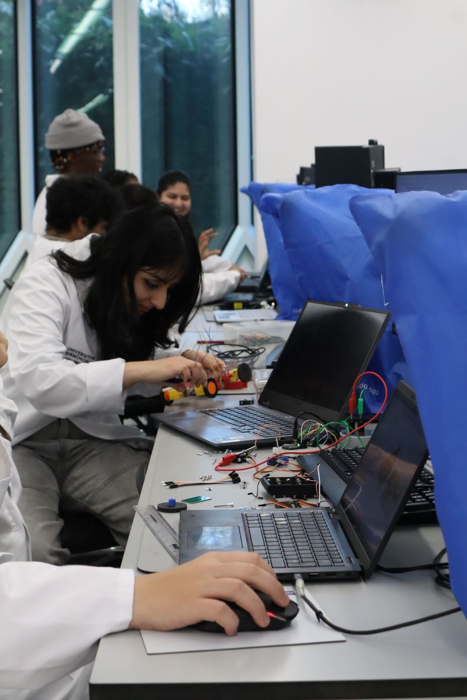 Students assembling electronics and a wheeled chassis at a bench.