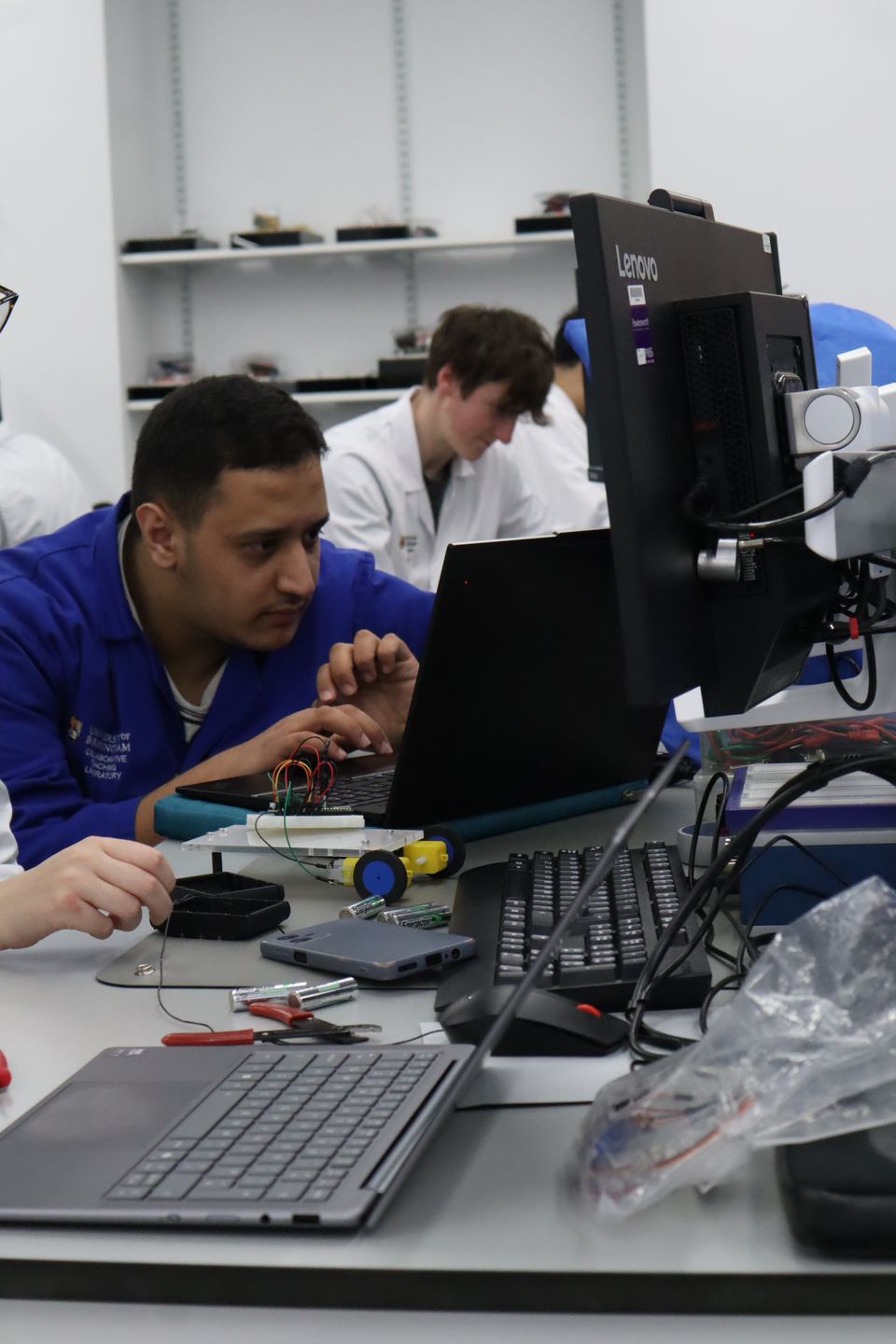 A student in a blue coat helping a participant with their project.