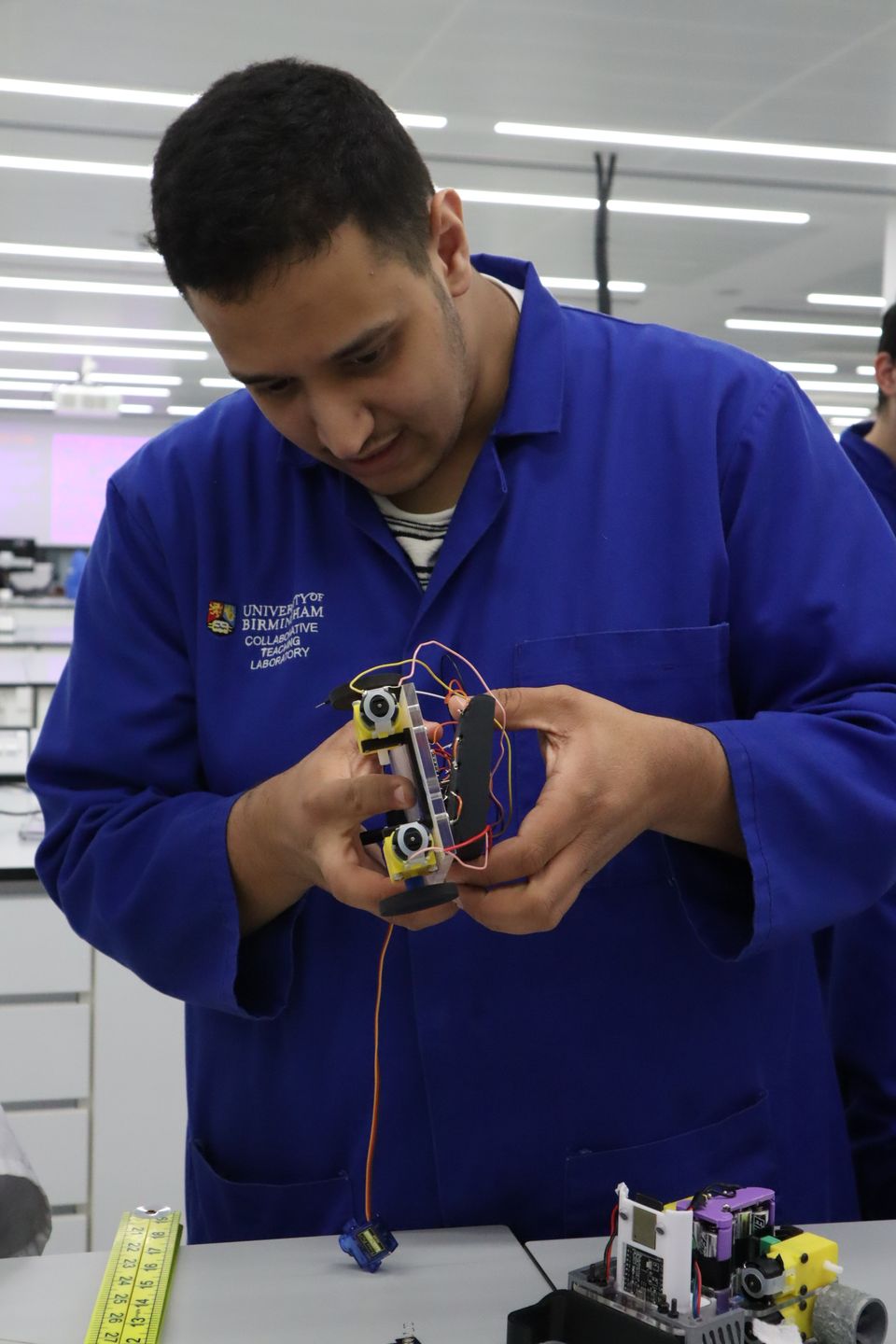 A student holding a small wheeled robot with visible wiring.