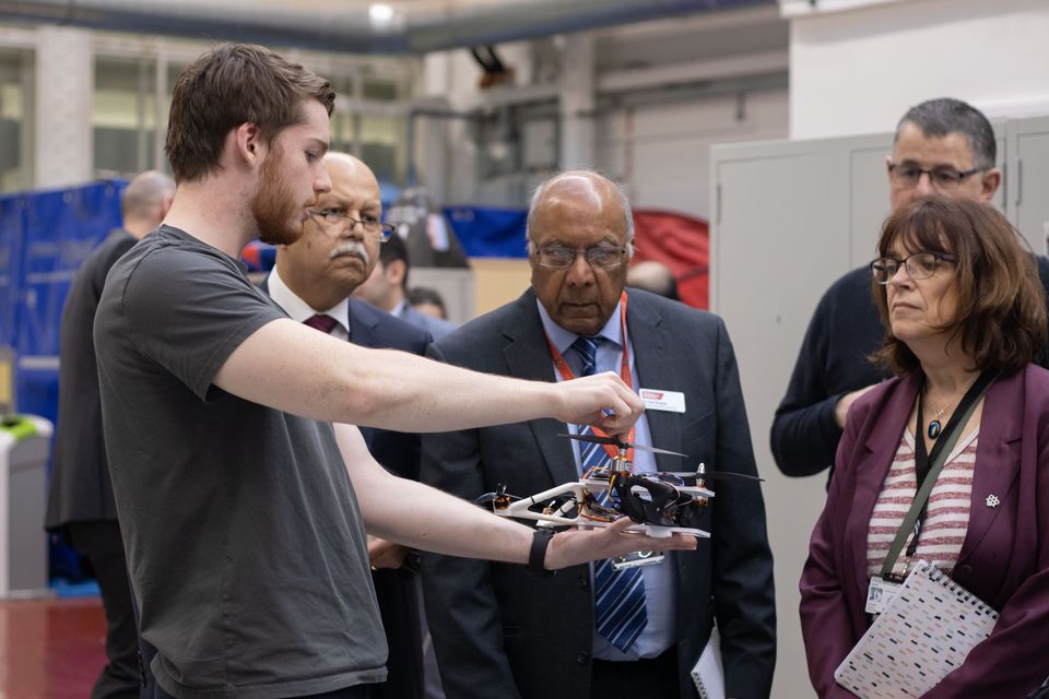 A student demonstrating a robot to visitors at a public event.