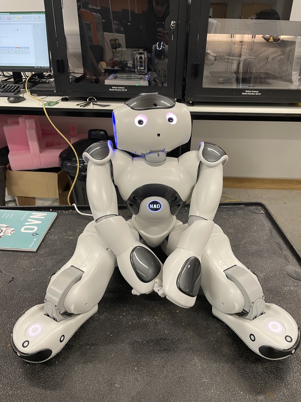 A white NAO humanoid robot seated on a workbench in the Makerspace.