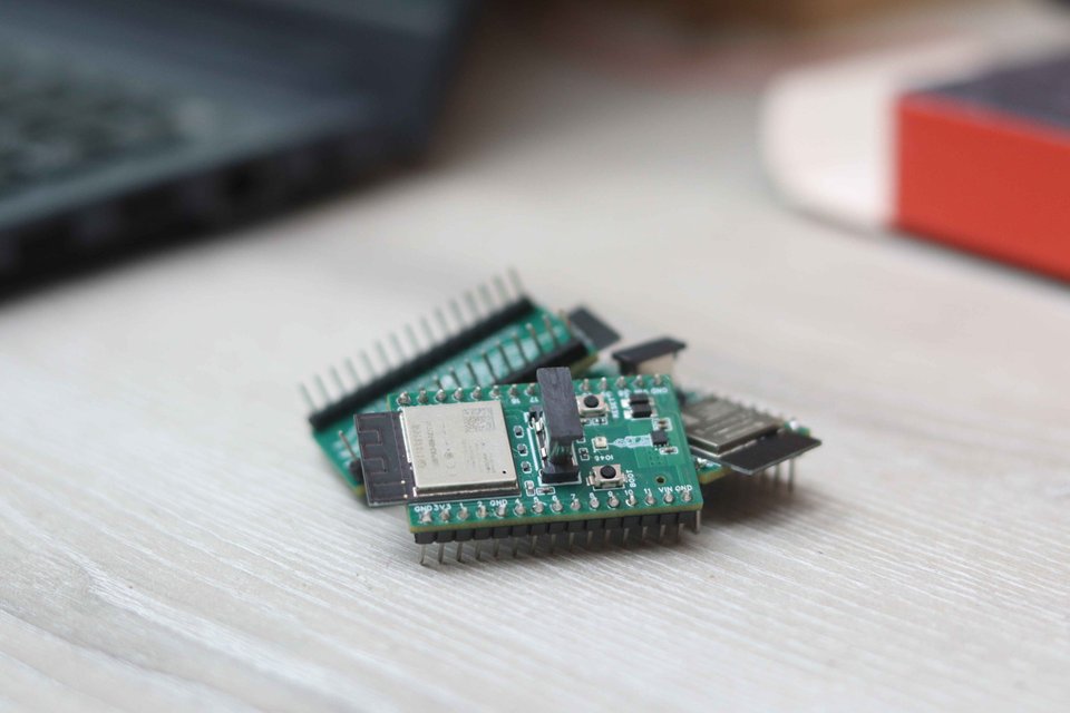 Two compact green microcontroller boards resting on a workbench.